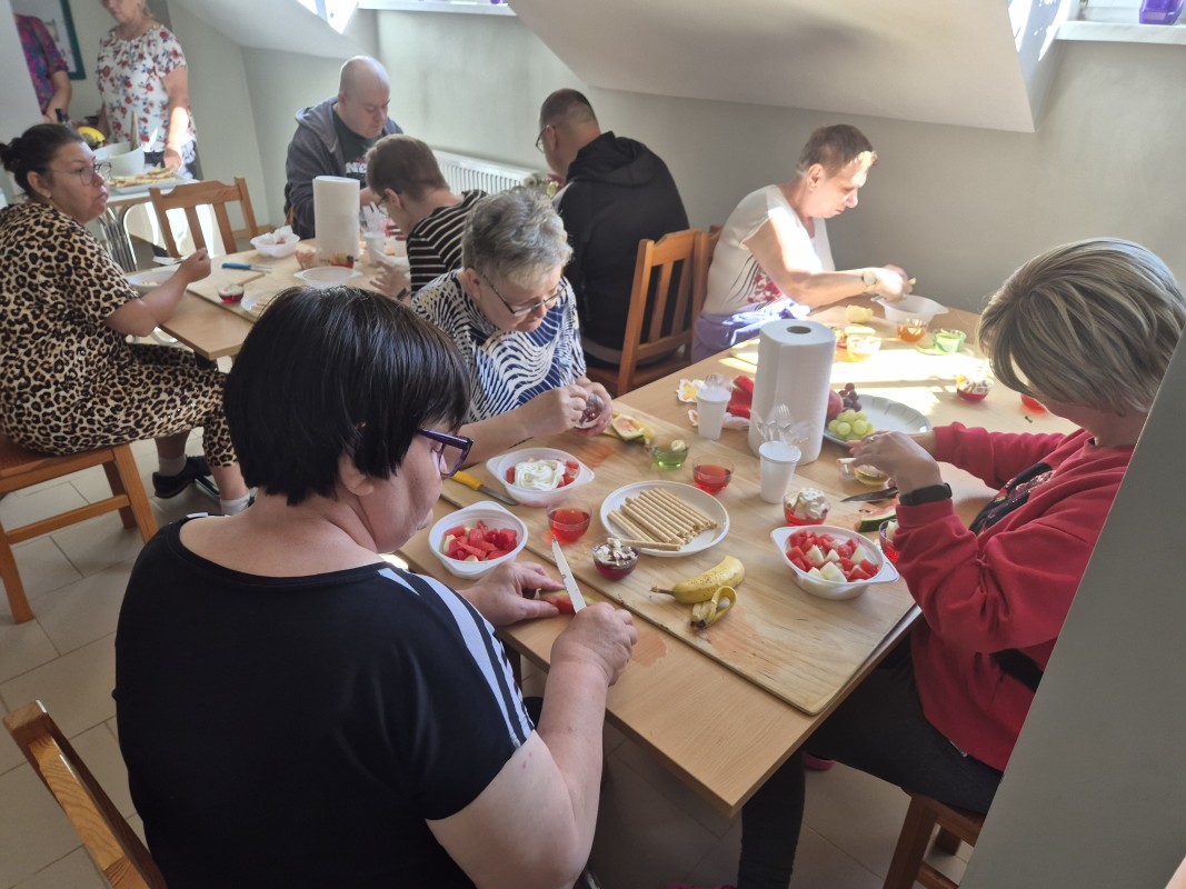 Warsztaty kulinarne. Grupa osób przygotowuje przy stole posiłek