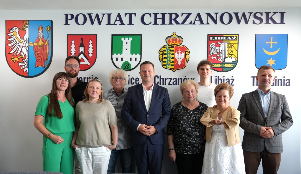 Członkowie rady stoją na tle ściany z napisem Powiat Chrzanowski oraz herbami gmin