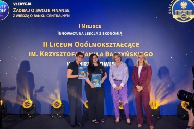 Kobiety stoją na tle tablicy informującej o konkursie
