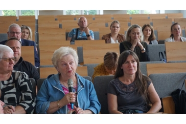 Zdjęcie dwunastu osób na sali wykładowej w różnym wieku i różnej płci. Jedna z pań trzyma mikrofon.