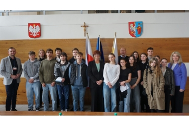 Zdjęcie kilkunastu osób w różnym wieku i płci. Głównie młodzieży. W tle 2 hebry (państwowy i powiatowy), krzyż oraz 3 flagi. 
