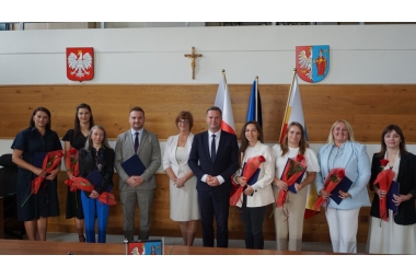 Zdjęcie dziesięciu osób stojących obok siebie, ustawionych do wspólnego zdjęcia. Na zdjęciu osiem kboeit i dwóch mężczyzn. Wszyscy elegancko ubrani. W tyle 2 tarcze w herbami, 3 flagi i krzyż.