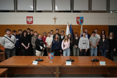Zdjęcie kilkudziesięciu uczniów wraz z trzema przedstawicielami urzędu. W tle herb powiatu, godło państwa oraz krzyż.