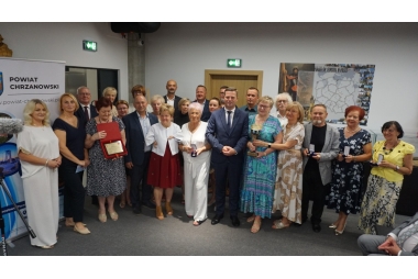 Zdjęcie kilkudziesięciu osób różnej płci i wieku stojący wspólnie do zdjęcia. Część z osób trzyma pudełka z medalami, patery lub statuetkę.
